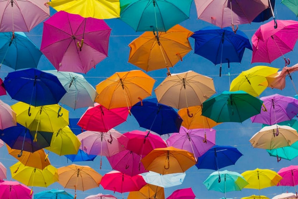Photograph of a bunch of colourful umbrellas hanging in the sky.